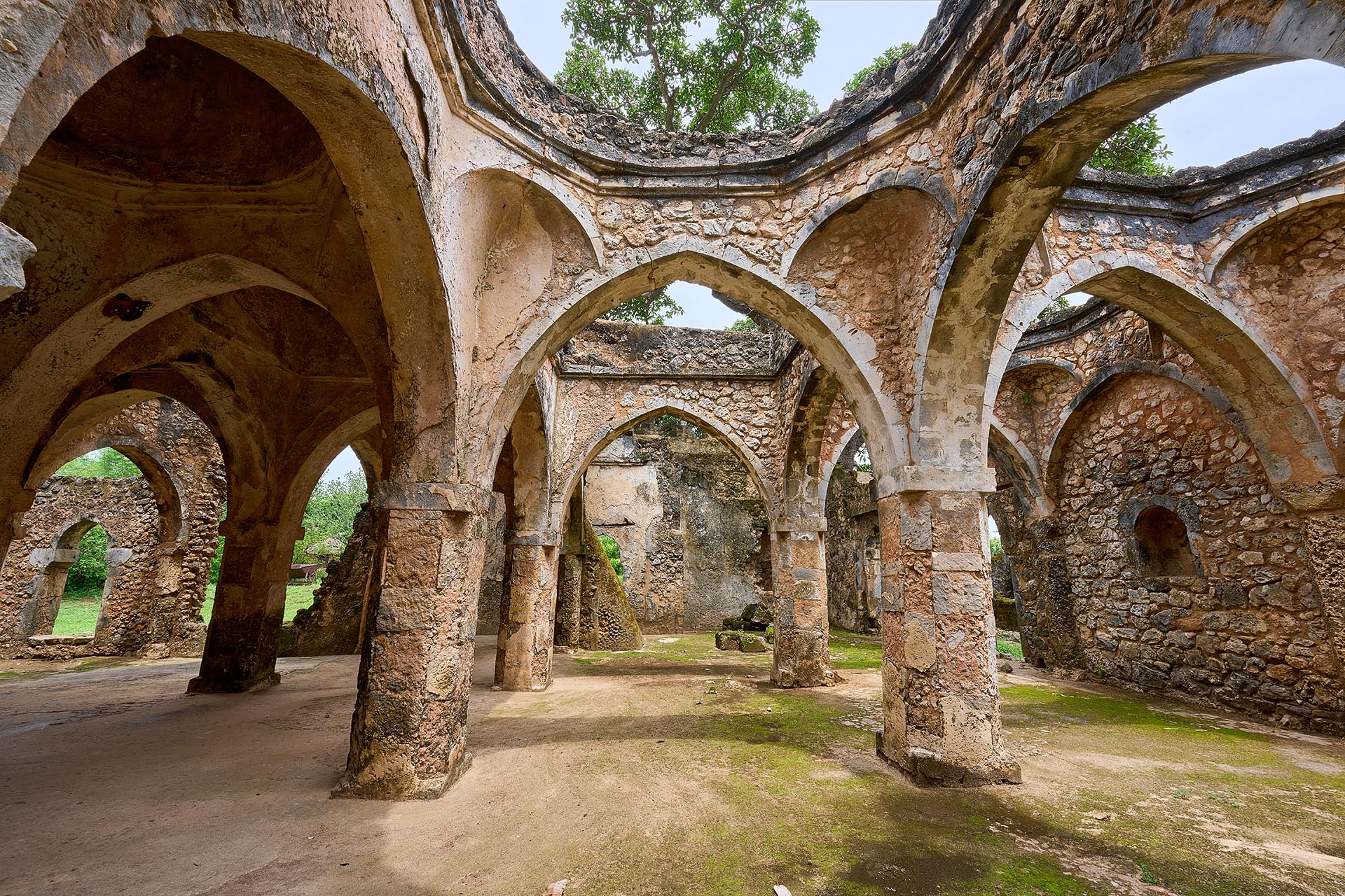 An image from the inside of The Great Mosque of Kilwa Kisiwani looking up at an angle to see the sky through the missing pieces of the dome. 