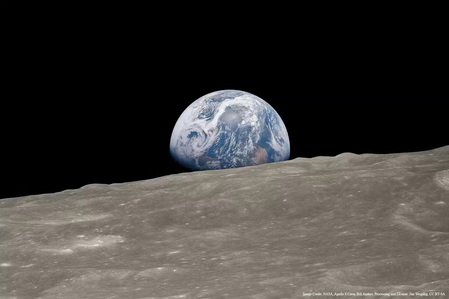 Looking at the Earth from the lunar surface. The surface is light in color and covered in craters.