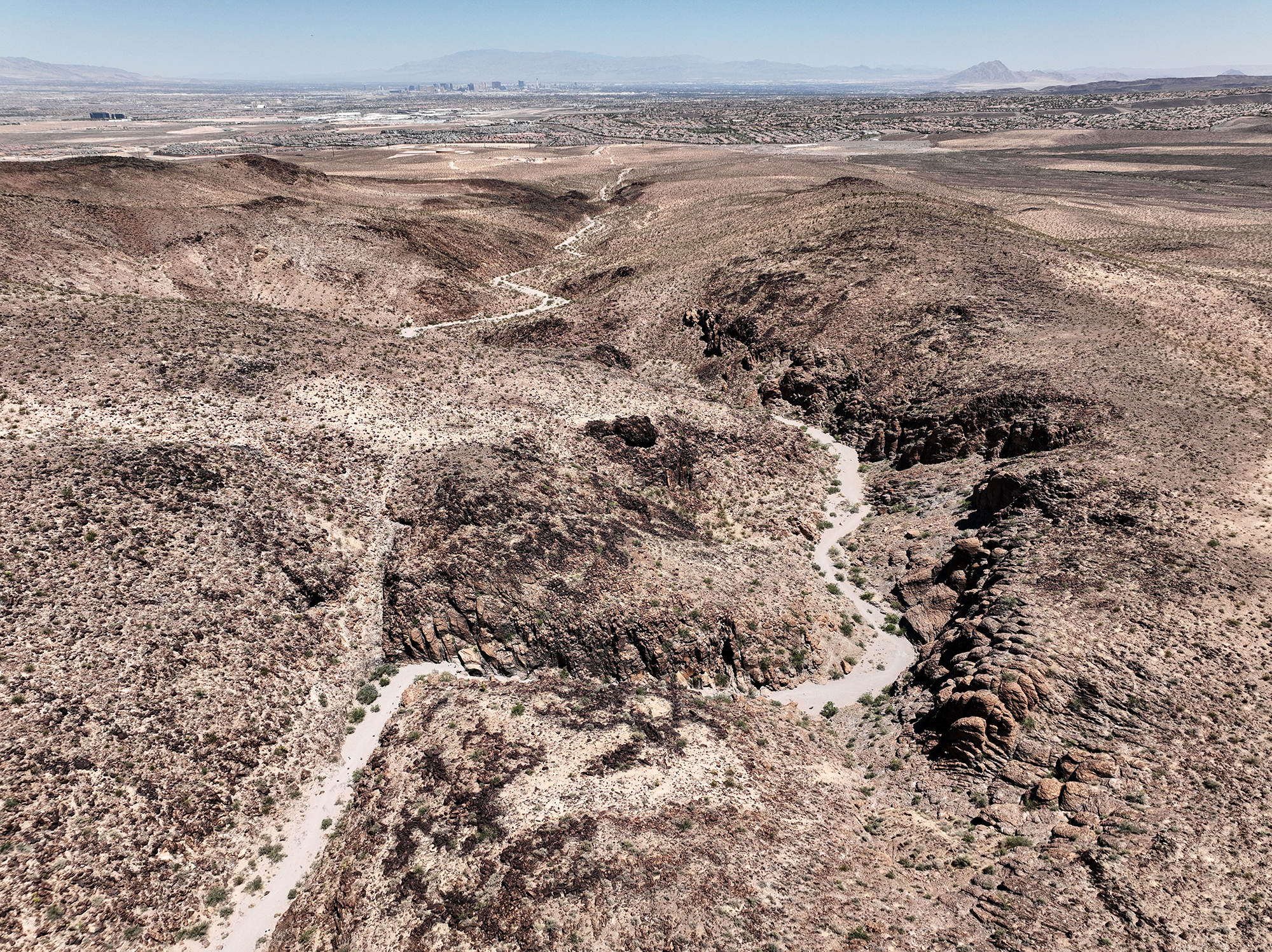 Brown desert mountains with a winding path leading to a city in the distance.